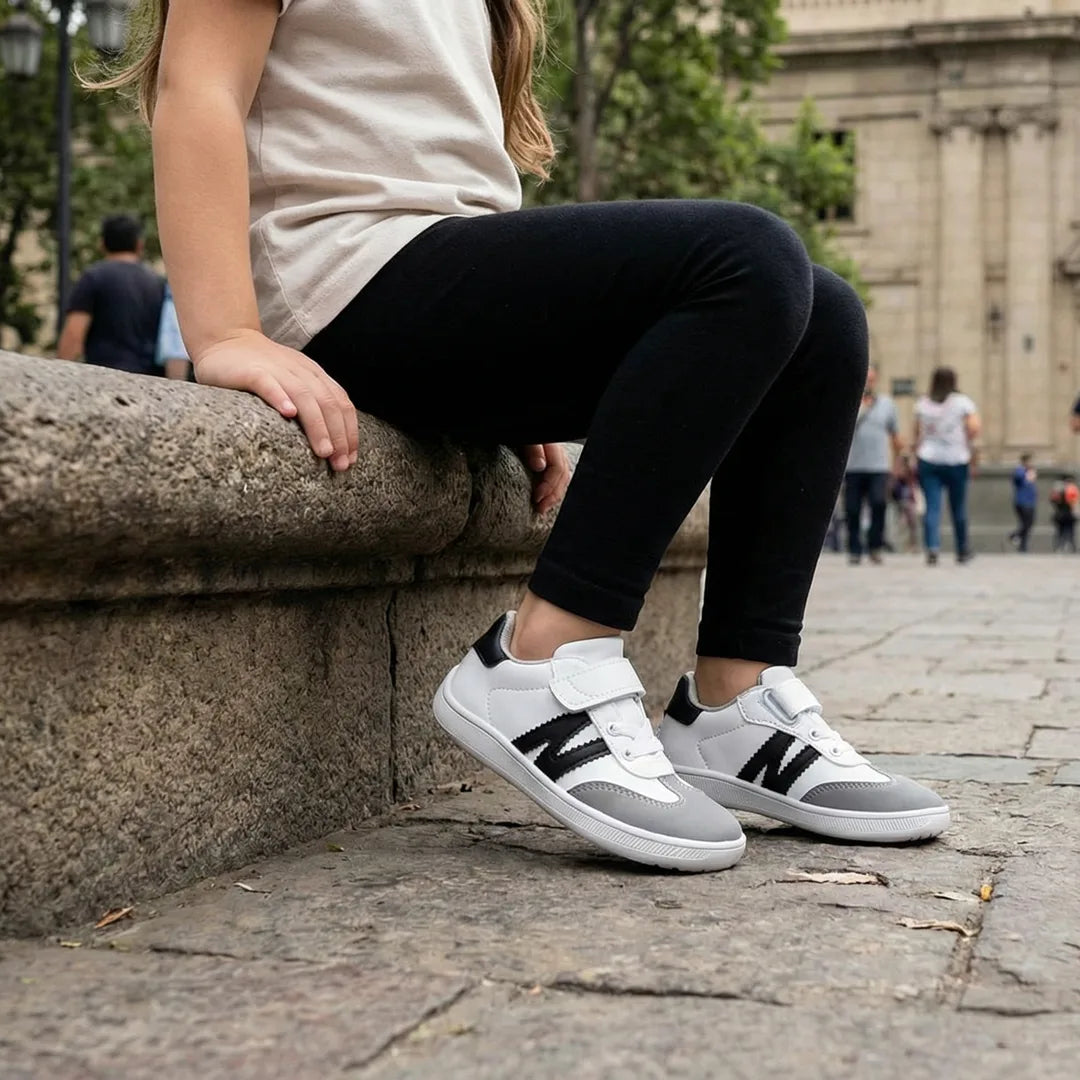 Niña sentada en una plaza usando zapatillas minimalistas ZZFaber Niza blanco/negro, calzado cómodo para juego diario en Chile.